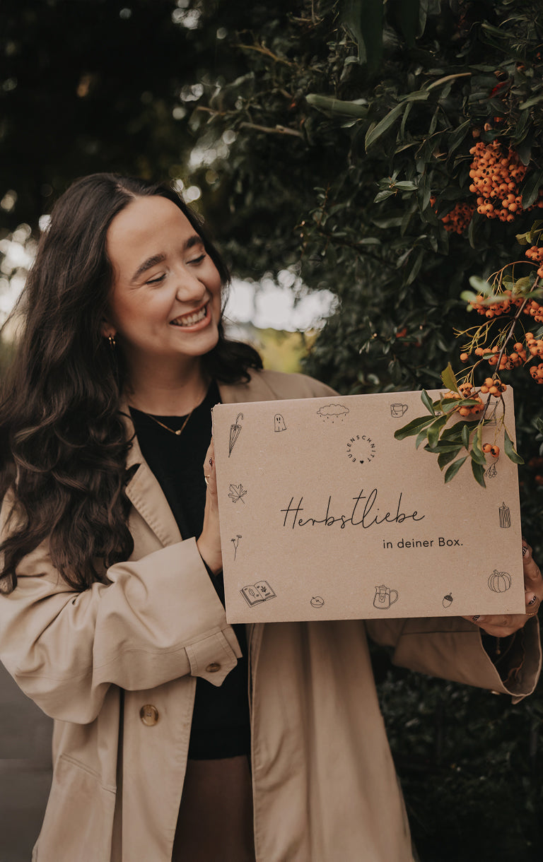 Frau im beigefarbenen Mantel hält lächelnd eine Herbstüberraschungsbox mit der Aufschrift: ‚Herbstliebe in deiner Box‘. Darüber steht: ‚Unsere Herbstbox – geht am 25.09.25 um 18 Uhr online!‘. Unten eine Schaltfläche mit der Aufschrift: ‚Überraschungsboxen‘ sowie der Hinweis: ‚Nur solange der Vorrat reicht!