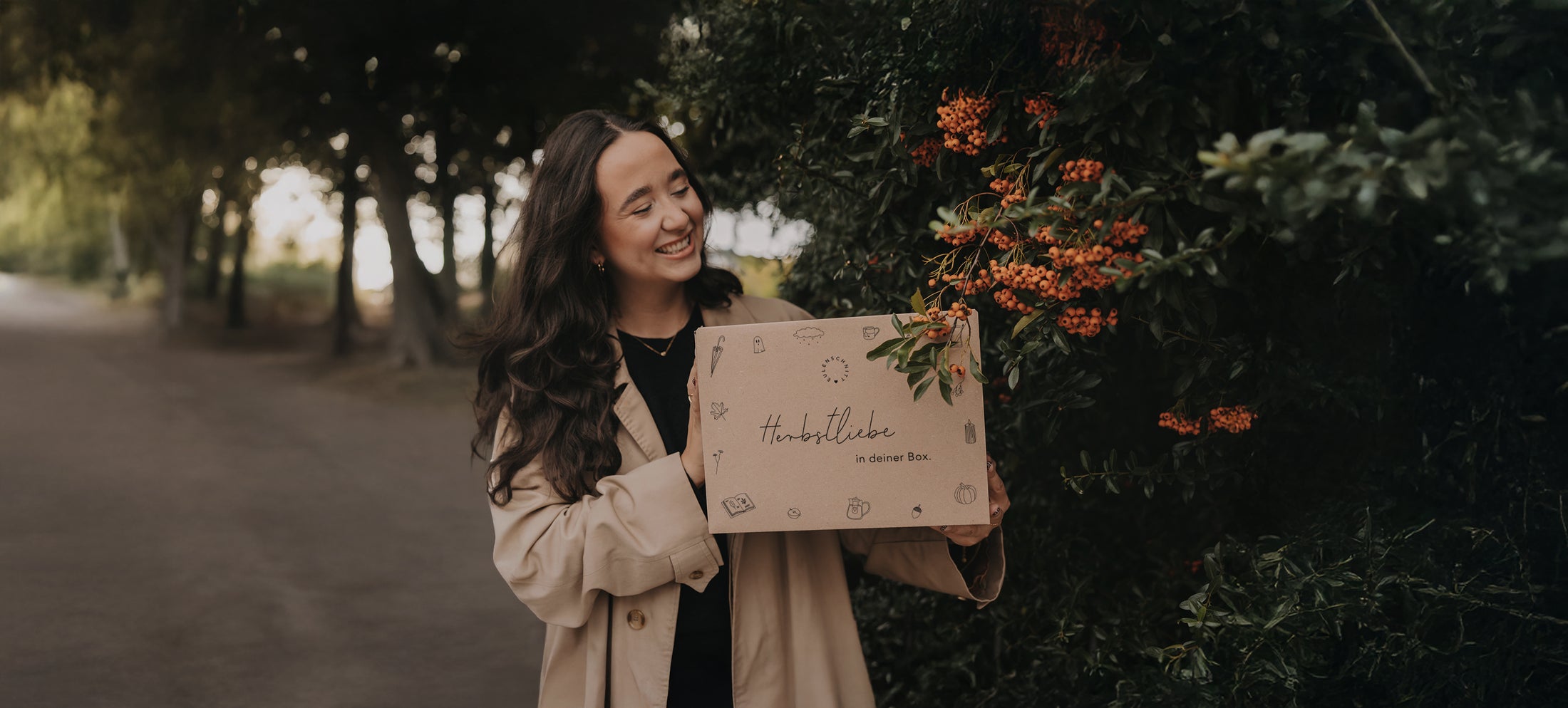 Frau im beigefarbenen Mantel hält lächelnd eine Herbstüberraschungsbox mit der Aufschrift: ‚Herbstliebe in deiner Box‘. Darüber steht: ‚Unsere Herbstbox – geht am 25.09.25 um 18 Uhr online!‘. Unten eine Schaltfläche mit der Aufschrift: ‚Überraschungsboxen‘ sowie der Hinweis: ‚Nur solange der Vorrat reicht!