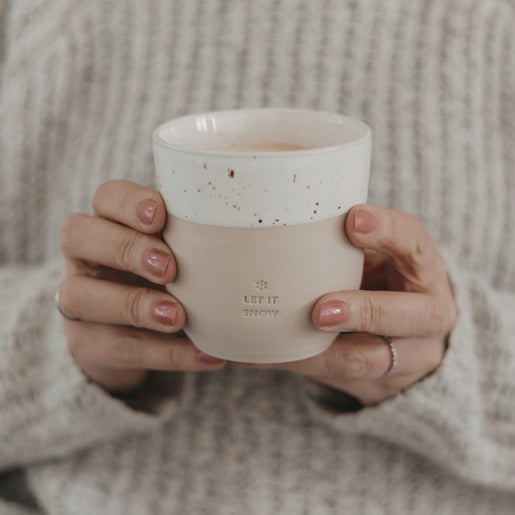 Nahaufnahme – Hände mit Steingutbecher „Let it Snow“