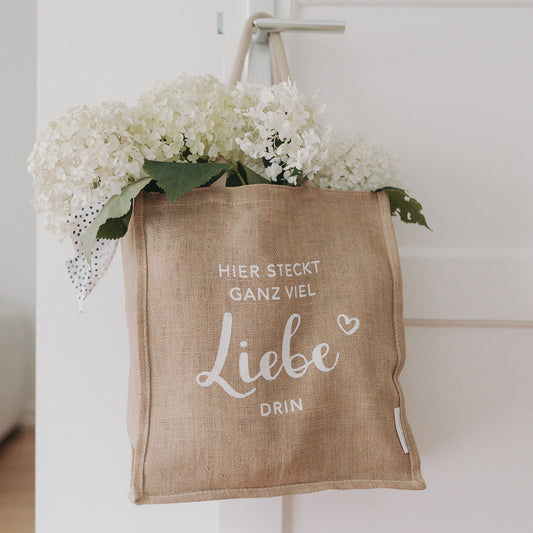 Die Tasche hängt an einem Haken, komplett zu sehen, gefüllt mit weißen Hortensien.