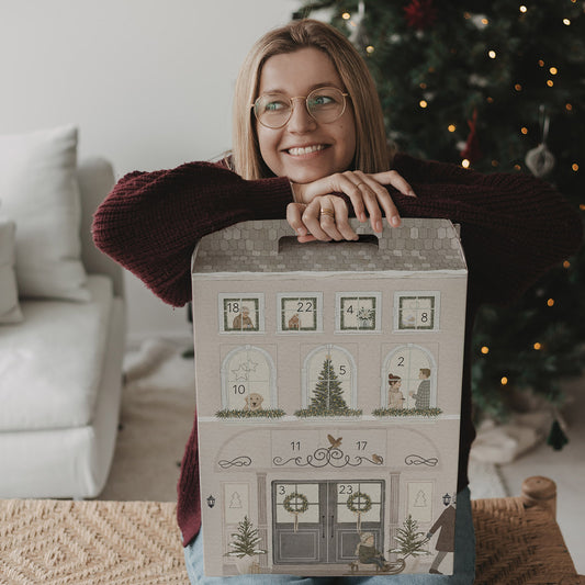 Frau lehnt lächelnd auf dem Eulenschnitt Signature-Adventskalender vor einem Weihnachtsbaum.