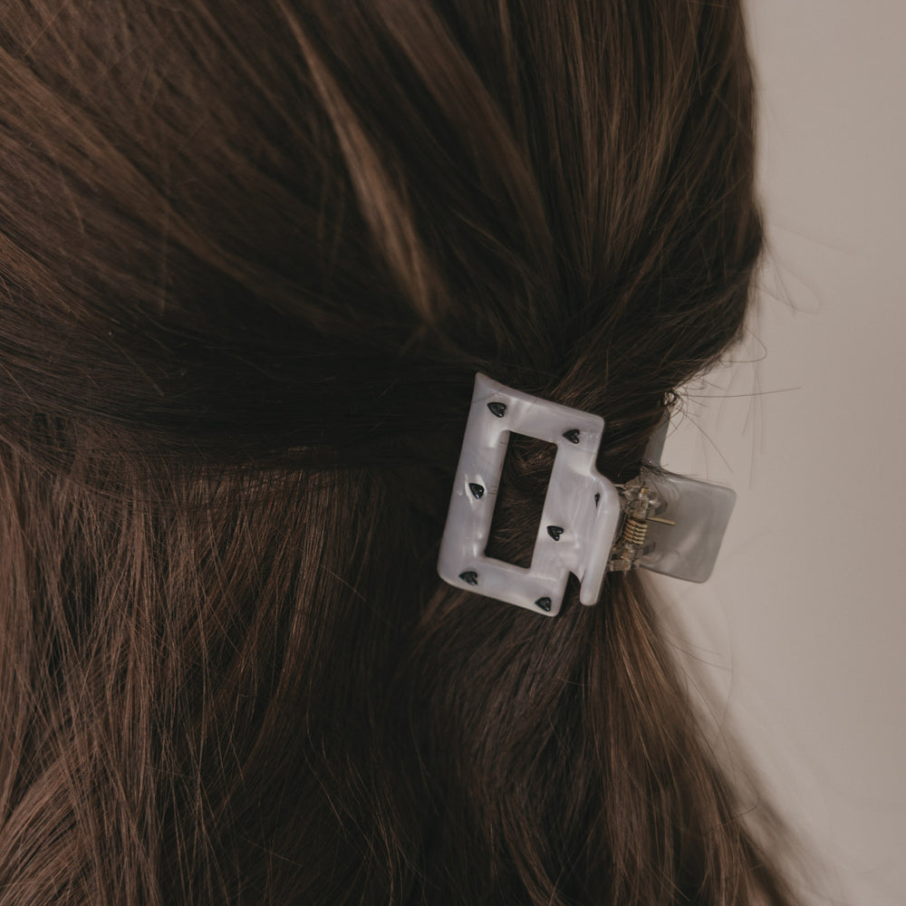 Kleine eckige Haarspange in Perlmutt-Optik mit schwarzen Herzen im halboffenen Haar