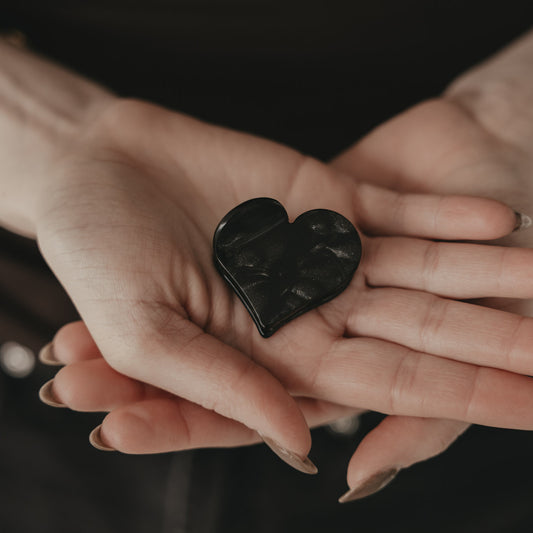 Große Haarspange in Herzform schwarz liegt in zwei Händen