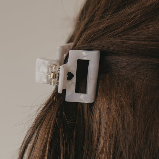 Kleine eckige Haarspange in Perlmutt-Optik mit schwarzem Herz im halboffenen Haar