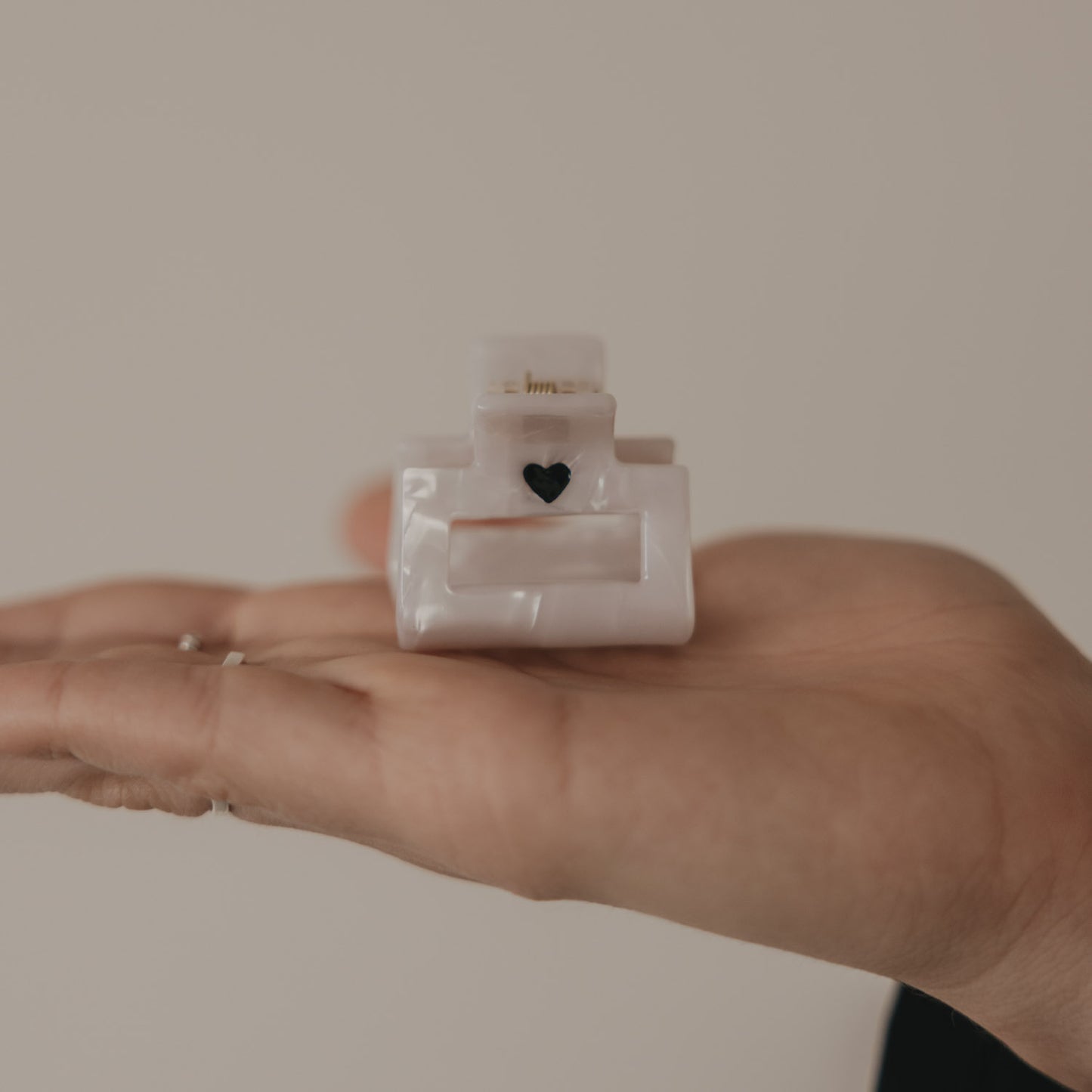 Kleine eckige Haarspange mit schwarzem Herz in Perlmutt-Optik in der Hand präsentiert