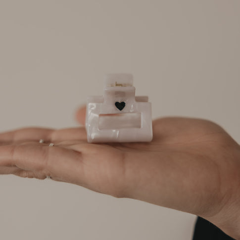 Kleine eckige Haarspange mit schwarzem Herz in Perlmutt-Optik in der Hand präsentiert