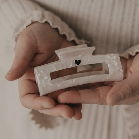 Maxi eckige Haarspange in Perlmutt-Optik mit schwarzem Herz in der Hand präsentiert