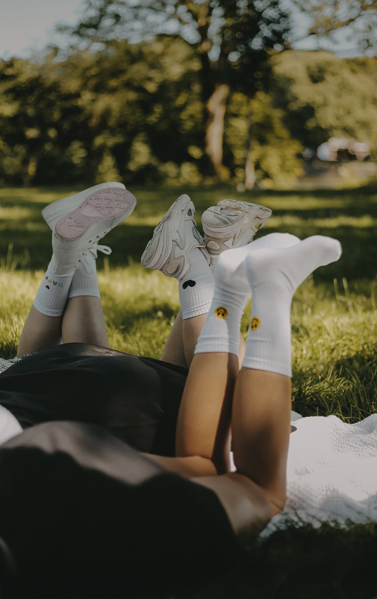 Drei Personen liegen entspannt auf einer Wiese im Park, die Beine in die Luft gestreckt. Die Szene ist sommerlich und locker mit Bäumen im Hintergrund. In weißer Schrift steht über dem Bild: „Sommersale –20 % auf alles“. Darunter der Hinweis: „Code: SOMMERBRISE“. Ein Sternchentext am unteren Bildrand informiert: „Gültig vom 12.07. bis 13.07.2025 | Rabatt wird nach dem Hinzufügen im Warenkorb abgezogen | Nicht kombinierbar mit anderen Rabatten.“