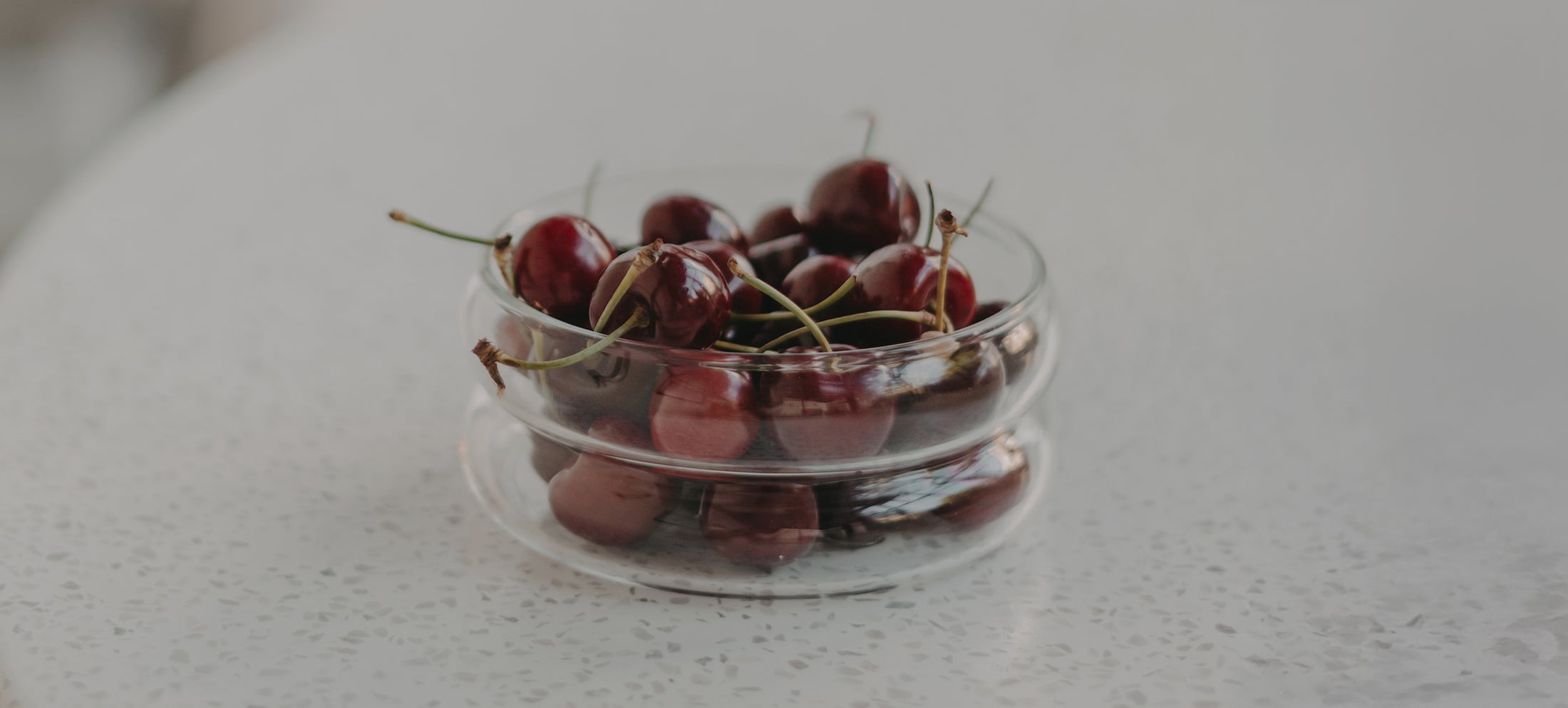 Schale in Bubble-Form aus Glas mit frischen, dunkelroten Kirschen auf einem hellen, strukturierten Untergrund.