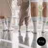 Familiensocken-Bundle in Weiß mit Aufdruck Mama, Papa und Mini – drei Paar Socken an Füßen von Eltern und Kind auf glänzendem Boden.