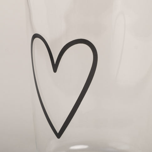Nahaufnahme vom schwarzen Herzmotiv auf klarem Trinkglas, minimalistisch und detailreich vor hellem Hintergrund gezeigt.