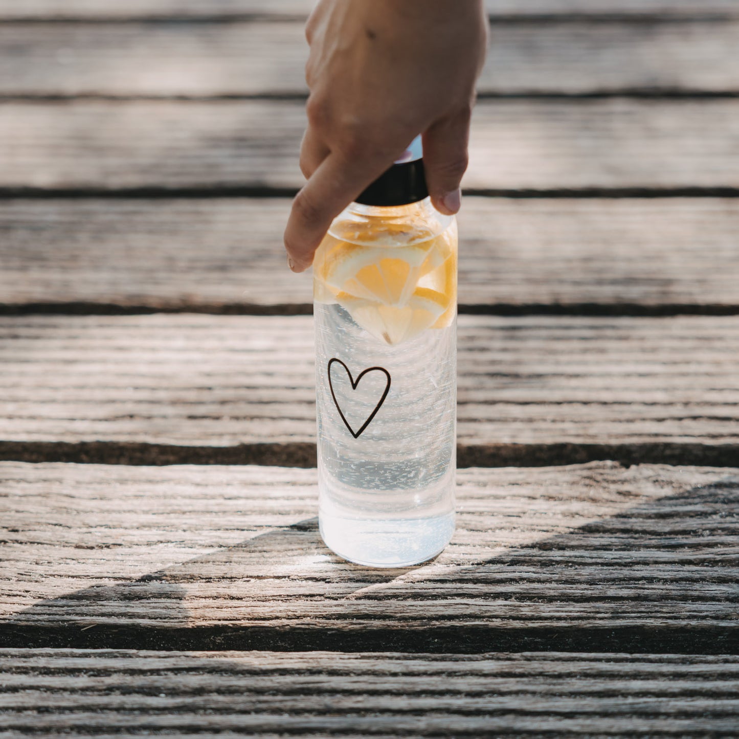 Glas Trinkflasche mit Herzprint und Zitronen wird auf Holzoberfläche abgestellt