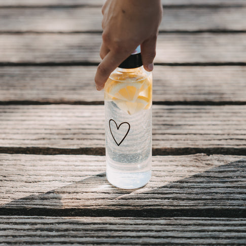 Glas Trinkflasche mit Herzprint und Zitronen wird auf Holzoberfläche abgestellt