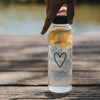 Transparente Glas-Trinkflasche mit schwarzem Herz, Wasser und Zitronenscheiben auf einem Holztisch
