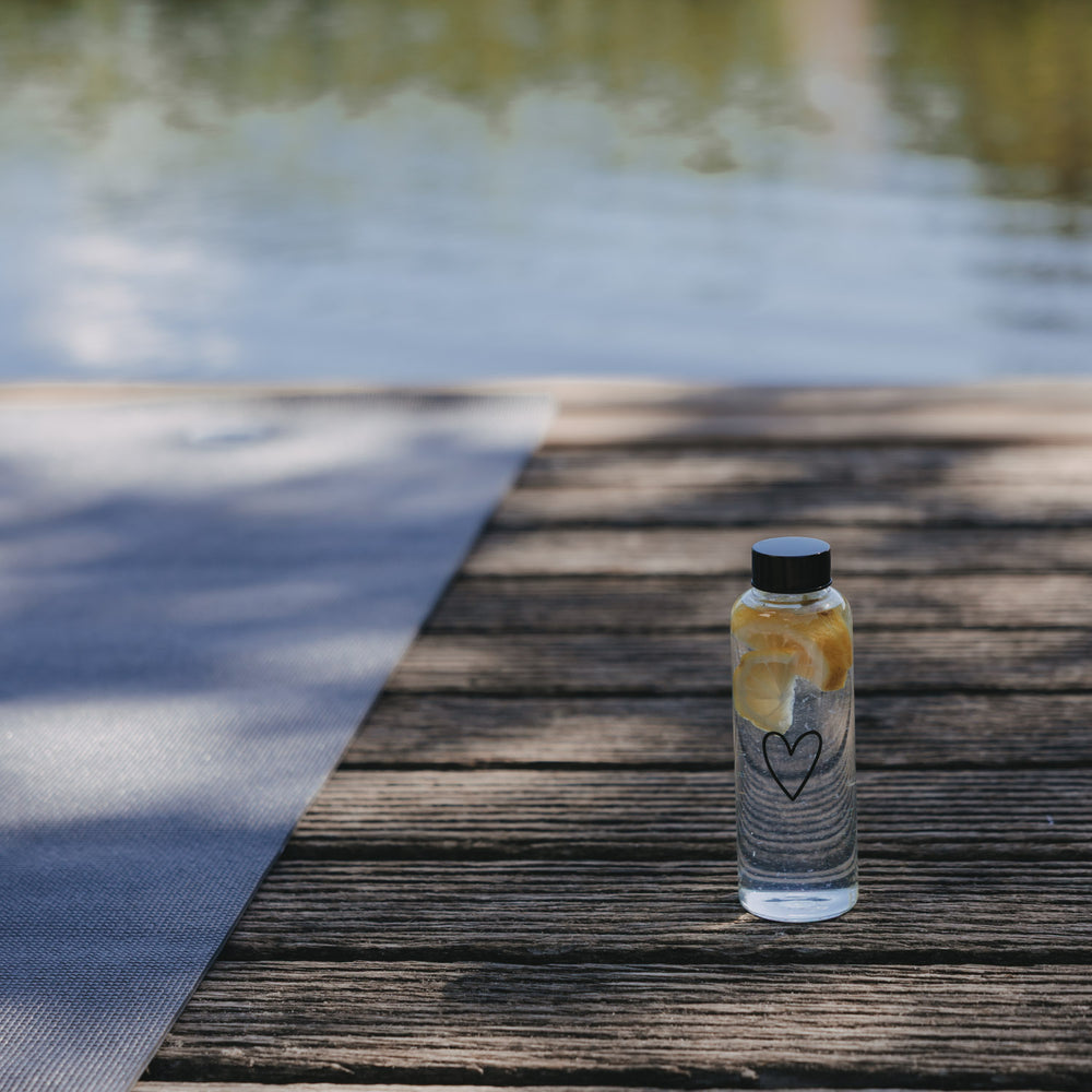Glas Trinkflasche mit Herzmotiv und Zitronenscheiben auf Holzsteg am Wasser