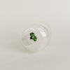 Figurglas mit grünem Kleeblatt im Inneren, transparentes Glas mit Eulenschnitt Logo auf hellem Hintergrund von unten fotografiert.