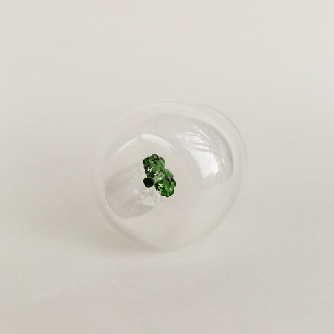 Figurglas mit grünem Kleeblatt im Inneren, transparentes Glas mit Eulenschnitt Logo auf hellem Hintergrund von unten fotografiert.