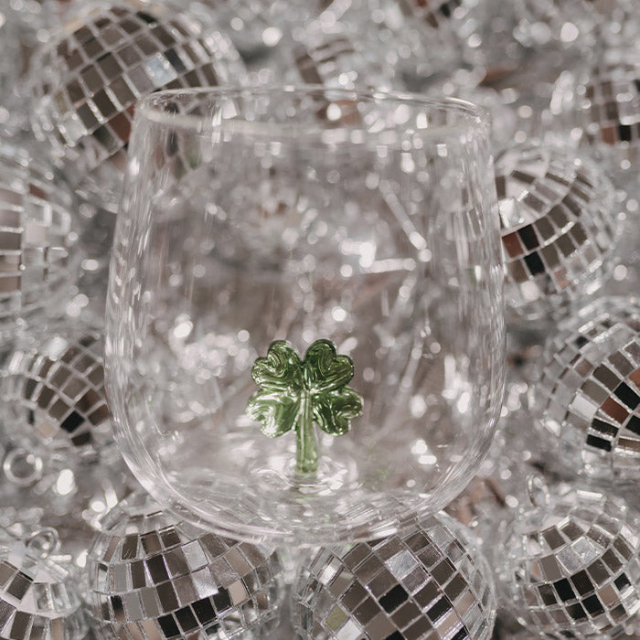 Transparentes Trinkglas mit kleiner grüner Kleeblattfigur im Inneren, umgeben von zahlreichen silbernen Discokugeln.