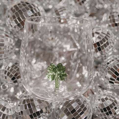 Transparentes Trinkglas mit kleiner grüner Kleeblattfigur im Inneren, umgeben von zahlreichen silbernen Discokugeln.