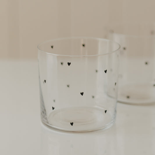 Transparentes Trinkglas mit kleinen schwarzen Herzen, im Hintergrund ein zweites passendes Glas
