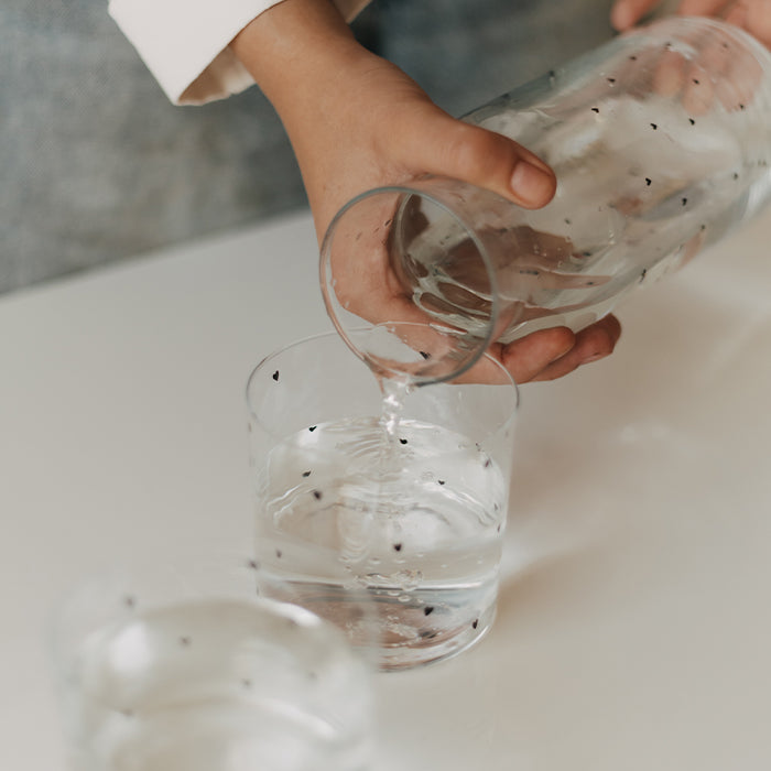Wasser wird aus einer Glaskaraffe mit kleinen schwarzen Herzen in ein passendes Trinkglas gegossen