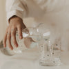 Wasser wird aus einer transparenten Herz-Karaffe in ein Trinkglas mit kleinen schwarzen Herzen eingeschenkt