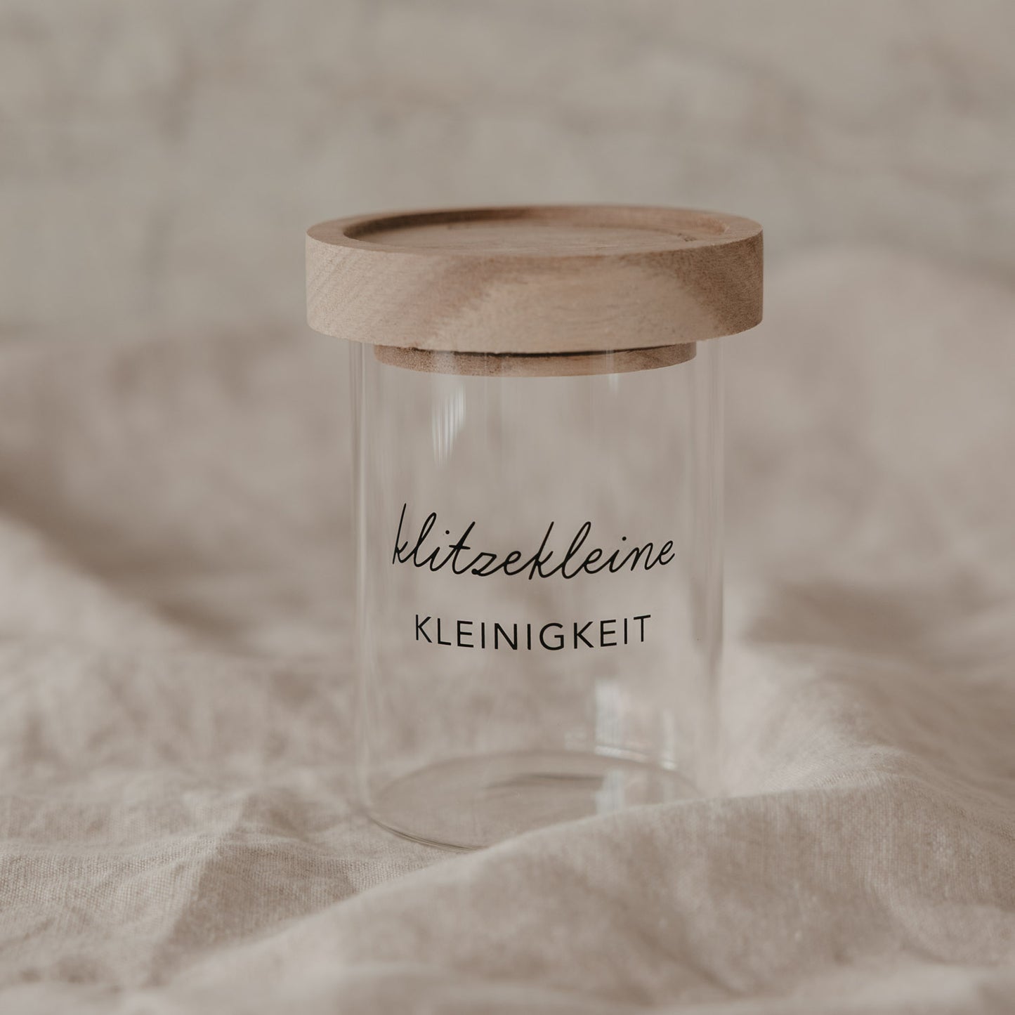 Minivorratsglas mit Holzdeckel und Schriftzug „klitzekleine Kleinigkeit“ auf hellem Stoff