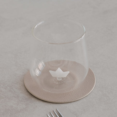 Transparentes Glas mit kleinem Papierboot im Inneren, dekorativ auf hellem Untergrund mit Geschirr arrangiert