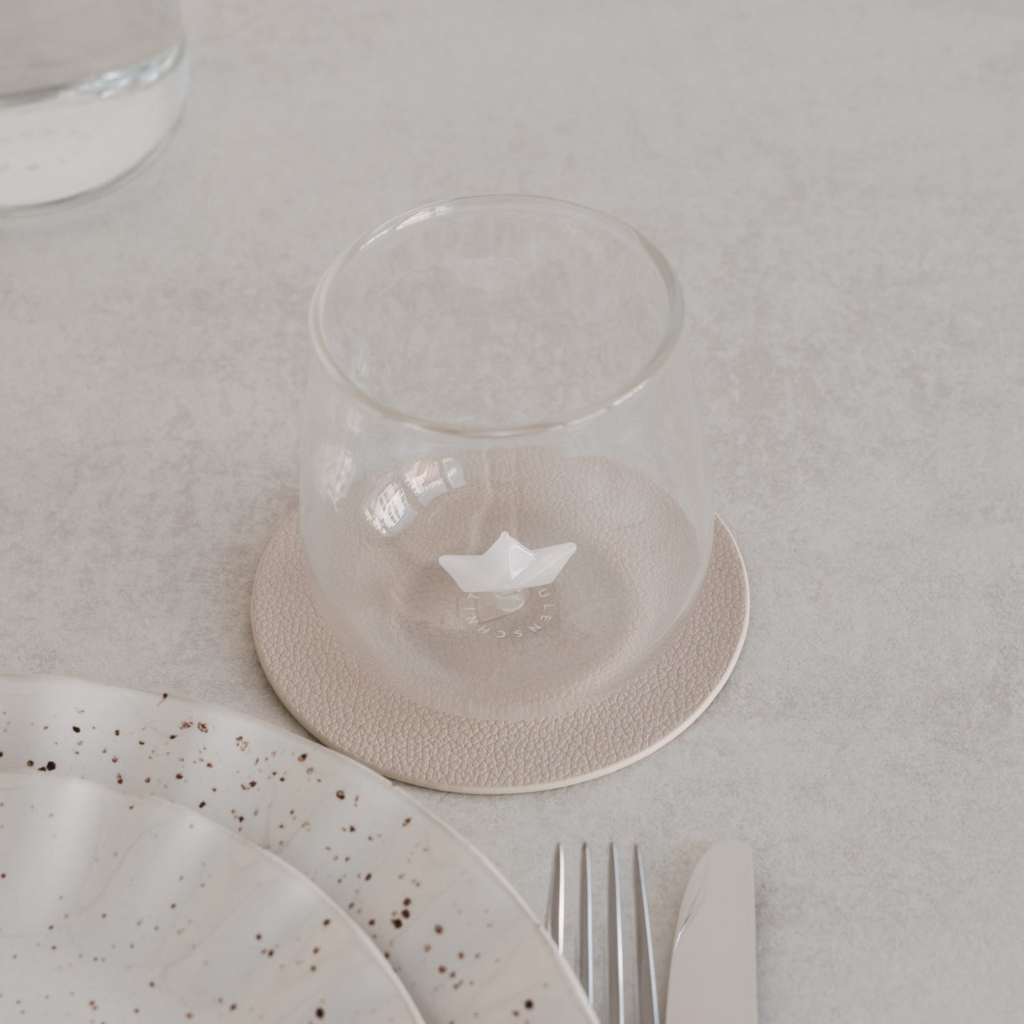 Glas mit Papierboot-Design, stilvoll inszeniert auf gedecktem Tisch mit Teller und Besteck