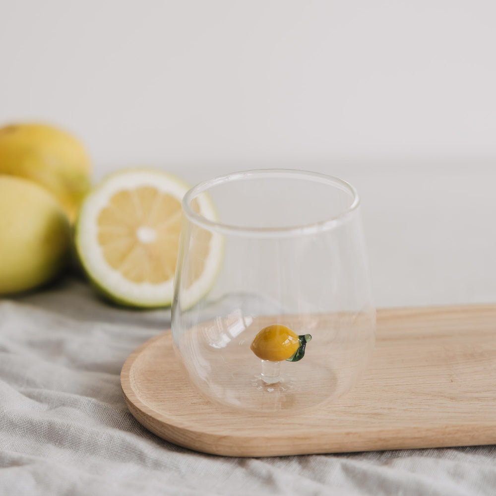 Trinkglas mit Zitronen Detail auf Holzbrett, dekoratives Glas mit frischen Zitronen im Hintergrund