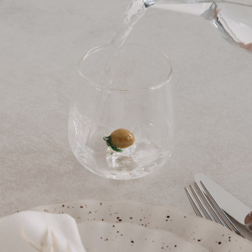 Zitronenfigur wird mit Wasser befüllt, modernes Designglas für Getränke auf gedecktem Tisch

