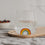 Trinkglas mit Regenbogen Motiv gefüllt mit Wasser, dekorativ auf Holzbrett arrangiert