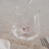 Trinkglas mit rosa Schwein im Boden, Wasser wird eingegossen, modernes Glasdesign