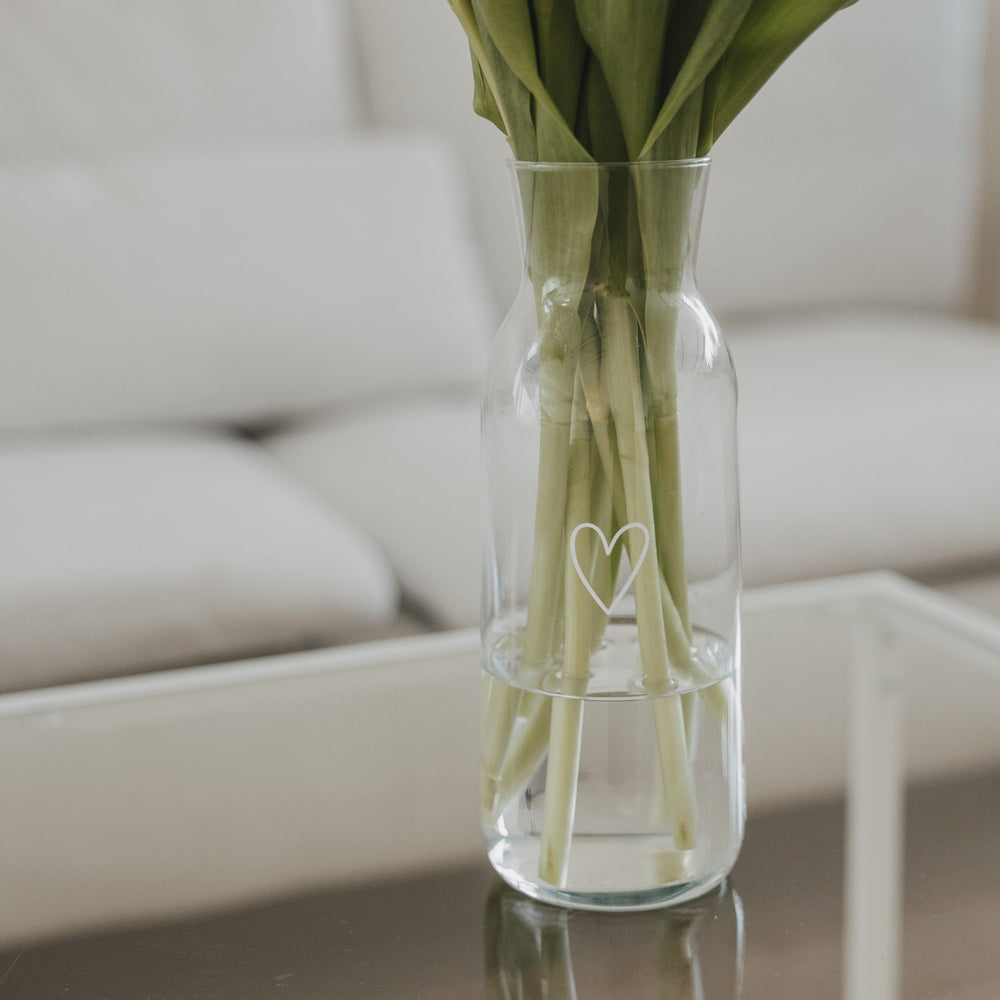 Glaskaraffe mit Tulpen und Herzmotiv, dekorativ auf Tisch platziert