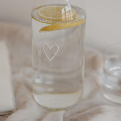 Glaskaraffe mit Wasser und Zitrone, kleines Herzmotiv, stilvolle Tischszene