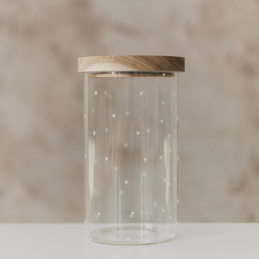 Vorratsglas mit weißen Herzen und rundem Holzdeckel vor beigem Hintergrund