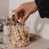 Hand greift nach Popcorn aus einem Glasbehälter mit kleinen schwarzen Herzen.