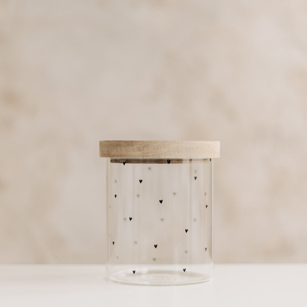 Leeres Vorratsglas mit kleinen schwarzen Herzen und aufgesetztem Holzdeckel vor hellem Hintergrund.