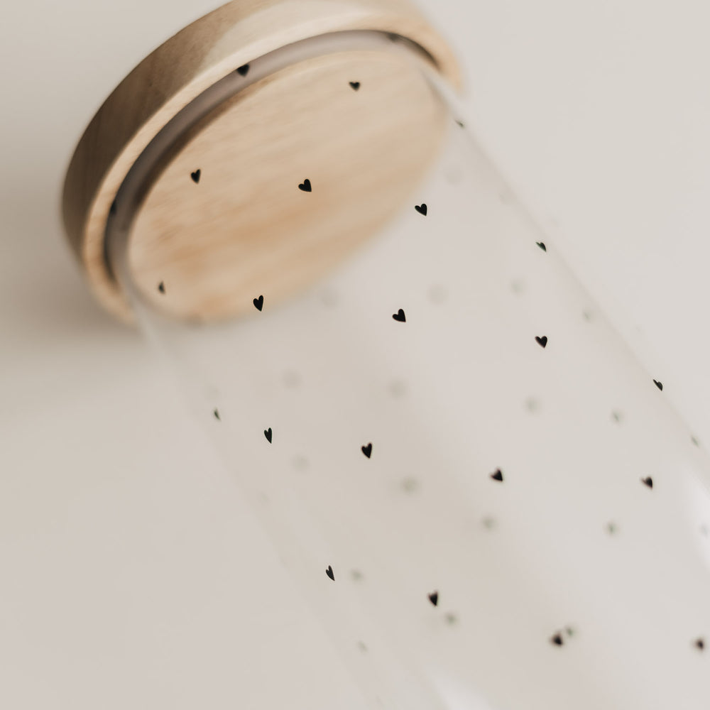 Detailaufnahme eines transparenten Vorratsglases mit schwarzen Herzchen und Holzdeckel.