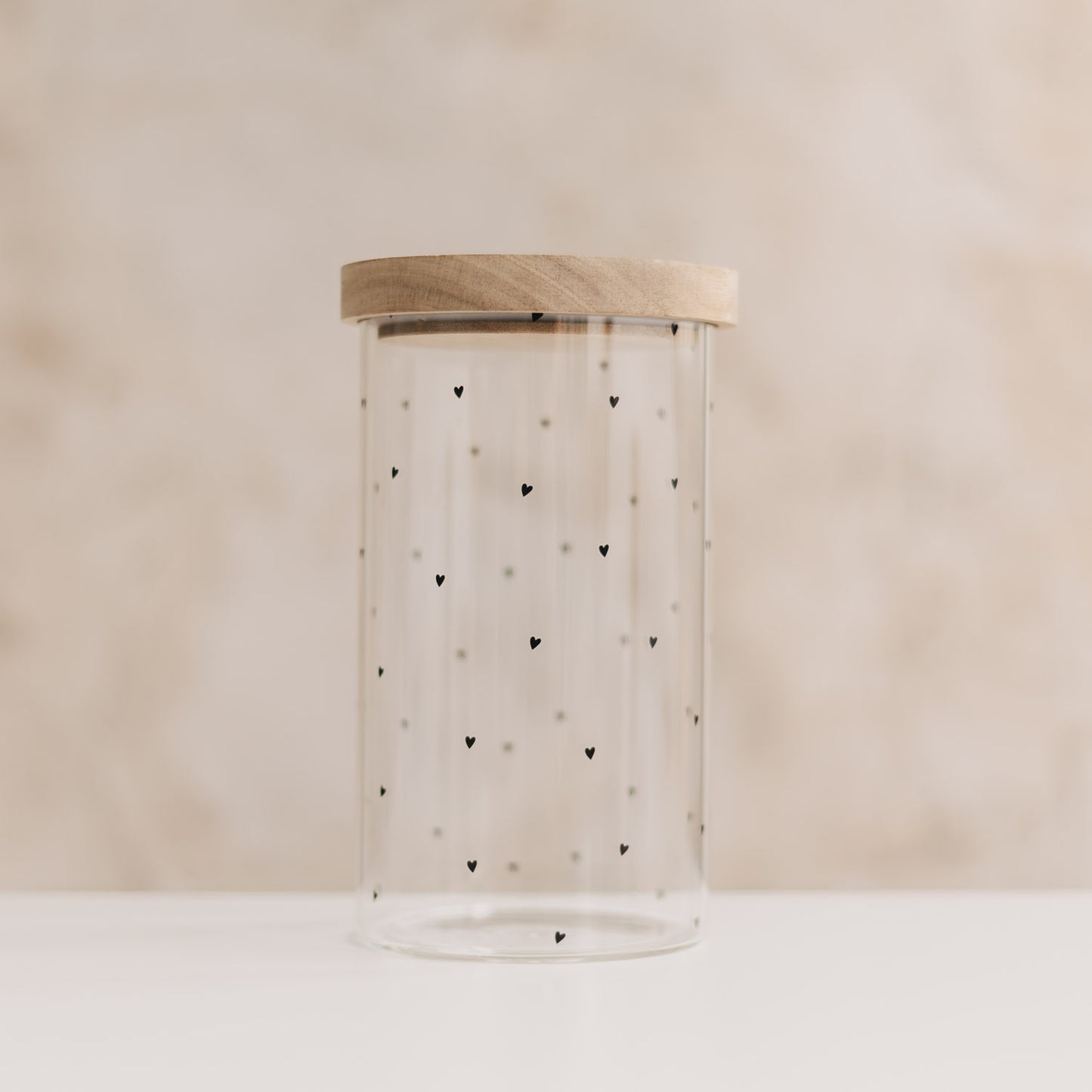 Leeres hohes Vorratsglas mit kleinen schwarzen Herzchen und geschlossenem Holzdeckel.