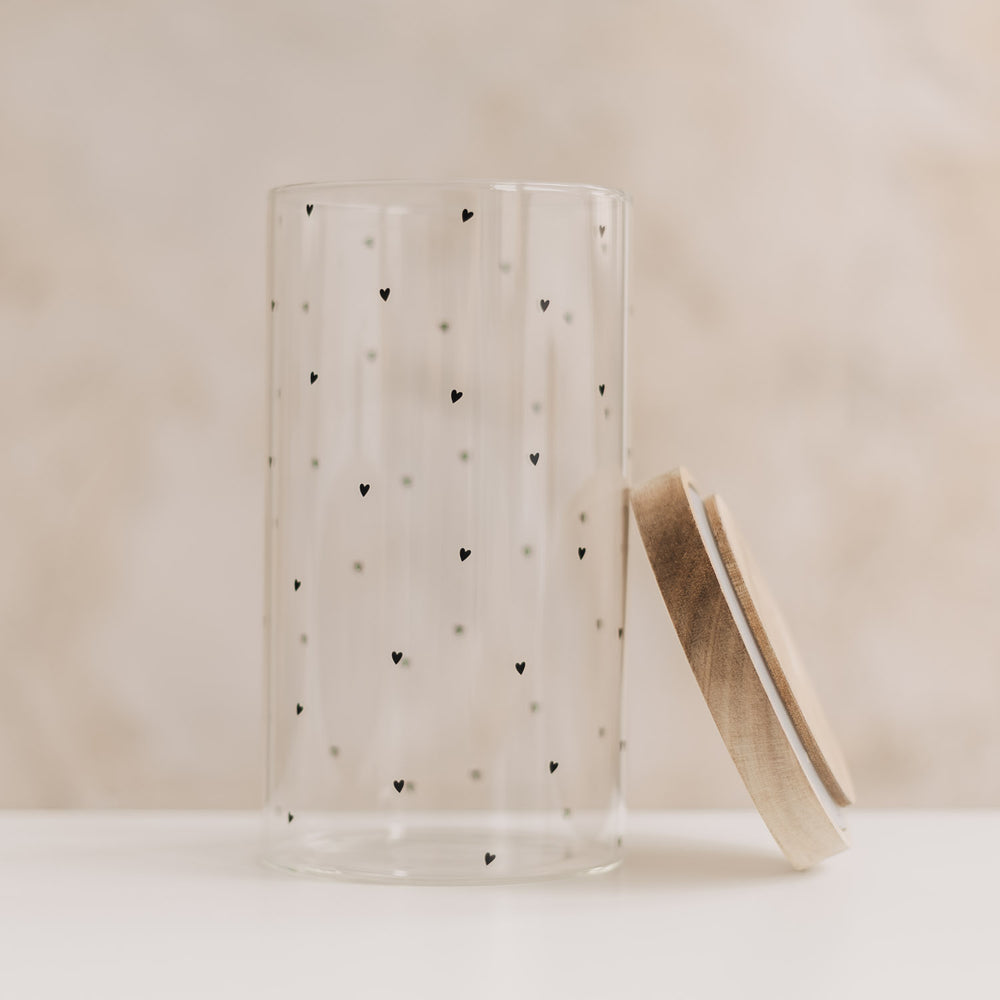 Leeres Vorratsglas mit schwarzen Herzchen und seitlich angelehntem Holzdeckel.