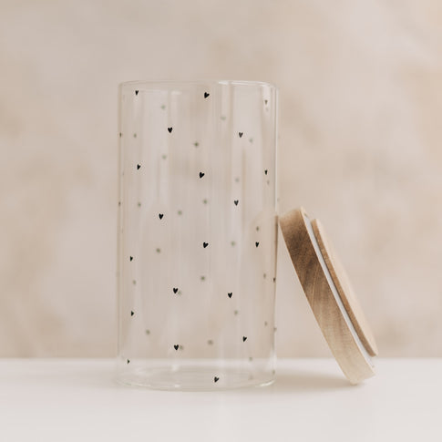 Leeres Vorratsglas mit schwarzen Herzchen und seitlich angelehntem Holzdeckel.