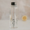 Glas Trinkflasche mit Blumenwiese Motiv, gefüllt, Zitrone im Hintergrund