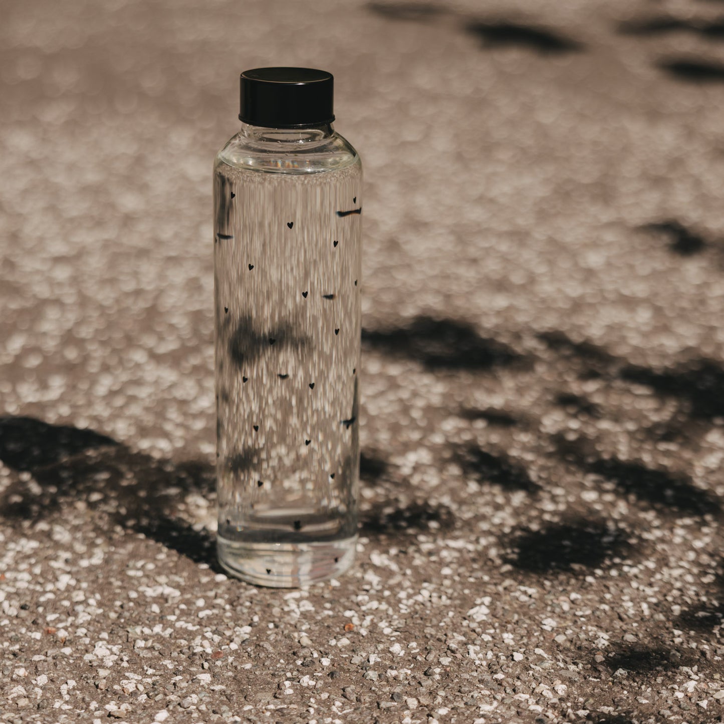 Glas Trinkflasche mit Herzmuster draußen im Sonnenlicht, schlicht und modern