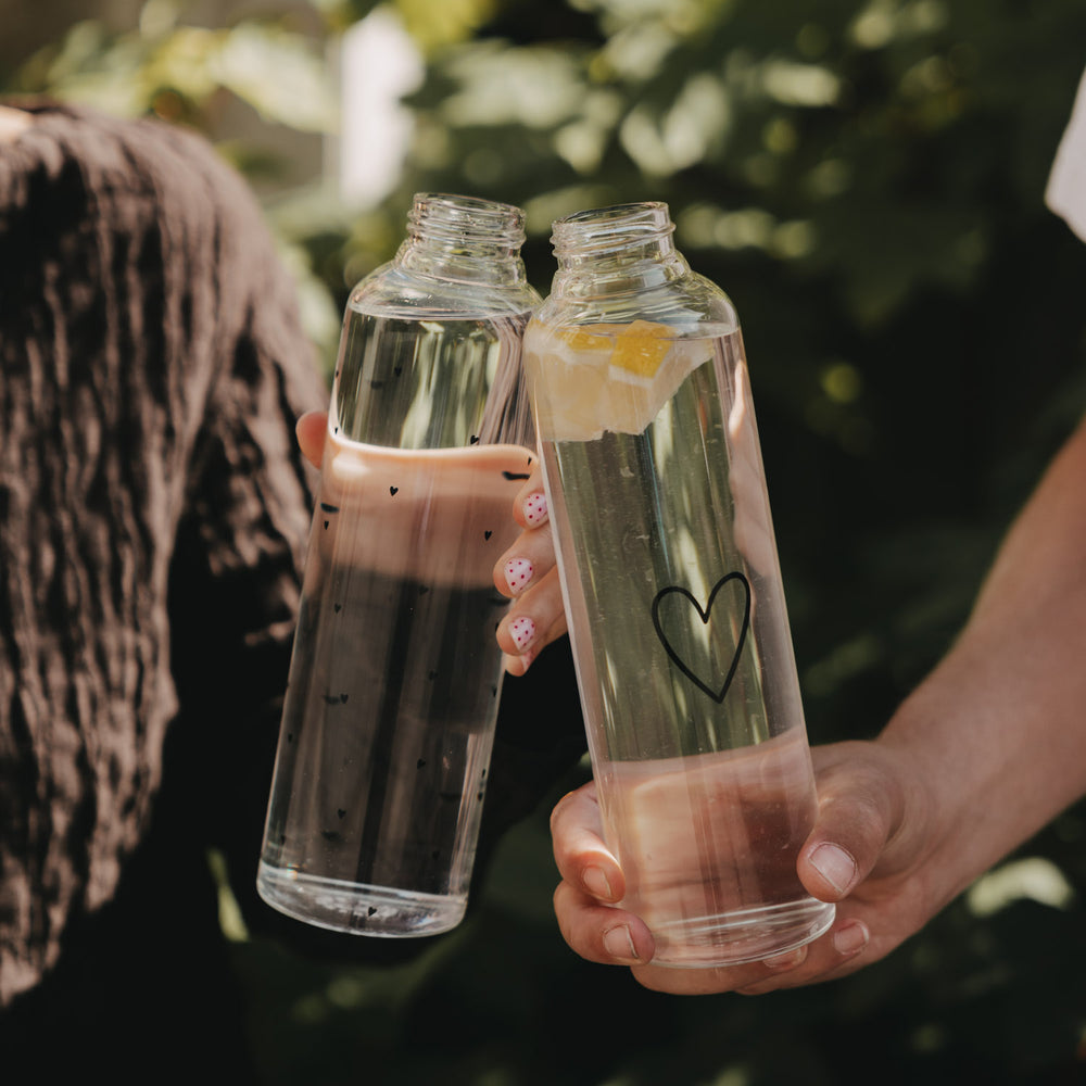 Zwei Trinkflaschen aus Glas mit Herzmotiv und Zitronenwasser in der Hand