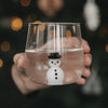 Figurenglas Schneemann mit Wasser gefüllt, in einer Hand vor warmen, weihnachtlichen Lichtern.