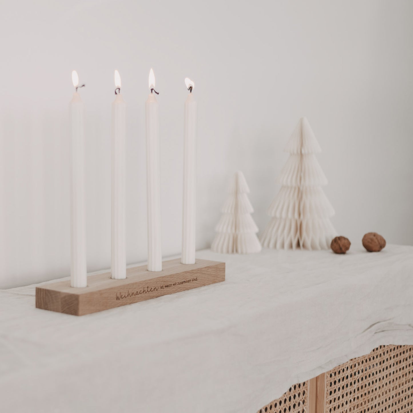 Weihnachtlicher Kerzenhalter mit vier Kerzen auf Tisch, im Hintergrund Papier-Tannenbäume