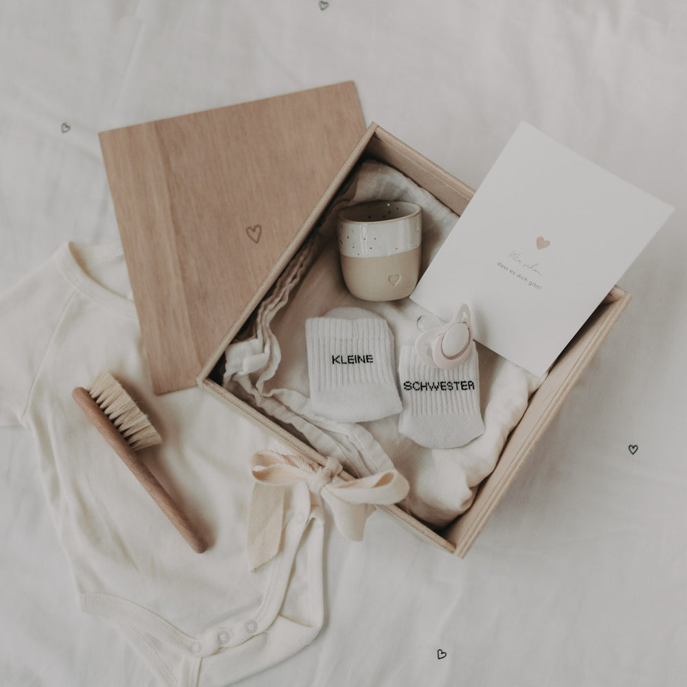 Geöffnete Erinnerungsbox Herz aus Holz, gefüllt mit Babyerinnerungen wie Söckchen, Karte und Tasse.