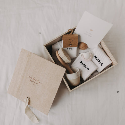 Gefüllte Erinnerungsbox mit Babyartikeln wie Socken, Bürste, Postkarte, Schnuller und Becher.