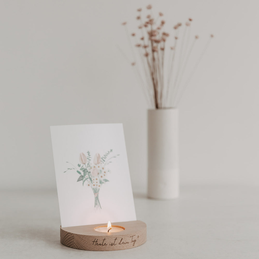 Dekorative Szene mit Holz-Kartenhalter „Heute ist dein Tag“, Teelicht und Blumenkarte im Hintergrund.